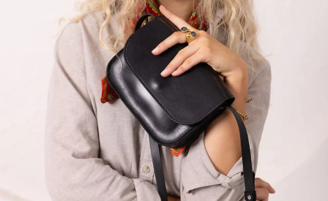 Modell hält kleine schwarze Leder-Crossbody-Tasche mit Umhängeriemen